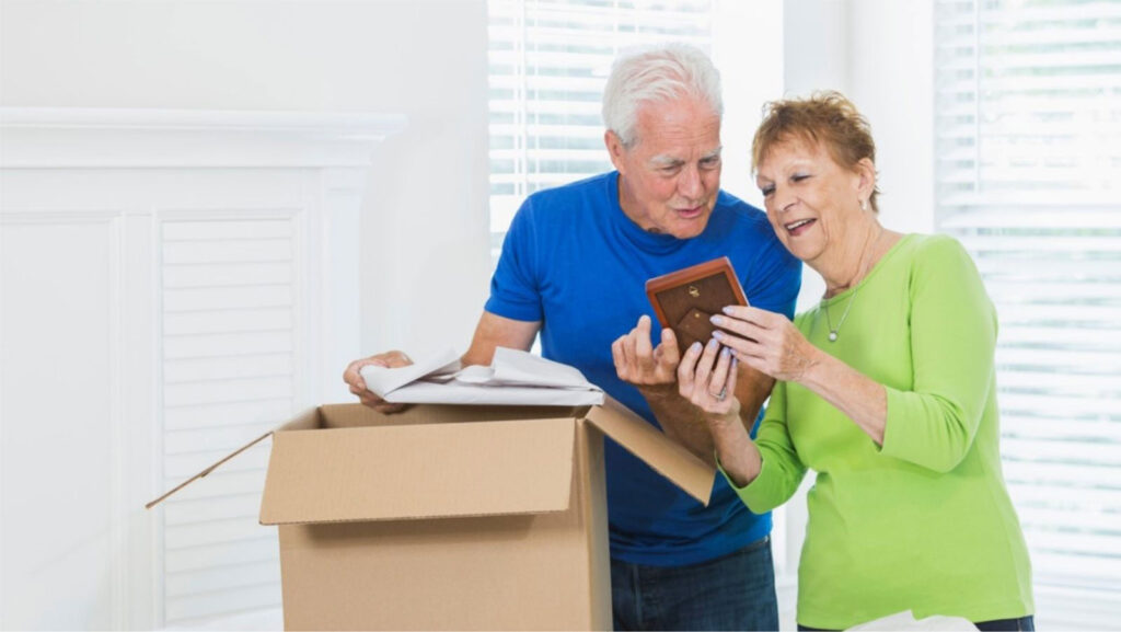 Senior man and woman standing over a cardboard box looking at an item